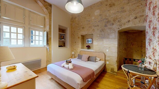 A bedroom with a stone wall, a bed with pillows, a bedside table with a lamp, and a chair.