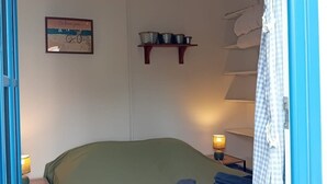 Una habitación con cama, repisa con utensilios de cocina, luz empotrada en la pared y una puerta con cortinas.