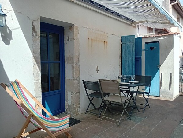 A small outdoor seating area with a table and chairs, a striped beach chair, and a blue door.