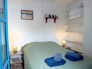 Una habitación con cama, una mesita de noche con lámpara, un estante con toallas y un cuadro en la pared.