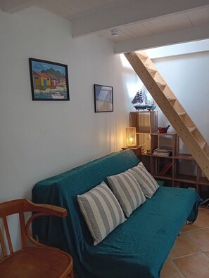 Una habitación con un sofá color turquesa, una silla de madera y una escalera.