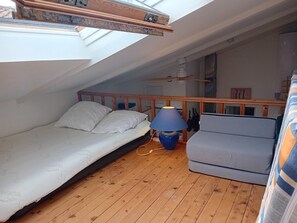 Una stanza piccola e accogliente con soffitto spiovente, un letto, un divano, una lampada e una ventola a soffitto.