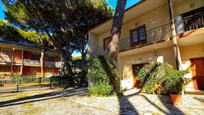 A courtyard with a stone pathway, potted plants, and a building with balconies. - Appartamento Puccini (Grosseto)