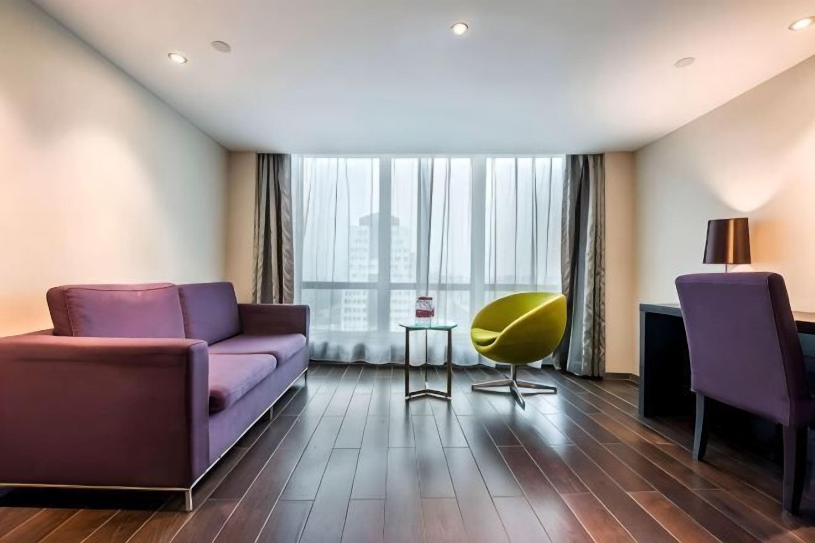 A modern room with a purple sofa, a yellow chair, a small table, and a lamp.