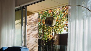 A modern hotel room with a large bed, a blue armchair, and a view of a garden through a sliding glass door.