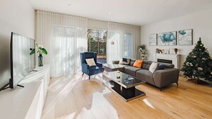 A modern living room with a flat-screen TV, a blue armchair, a grey sofa, and a glass coffee table.