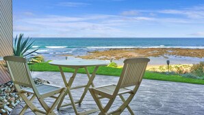 Un patio con una mesa y dos sillas que da a una playa rocosa y al océano.