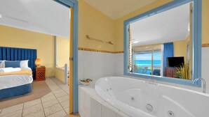 Habitación de hotel con una bañera grande, una cama con cortinas azules y vistas al océano a través de una ventana.