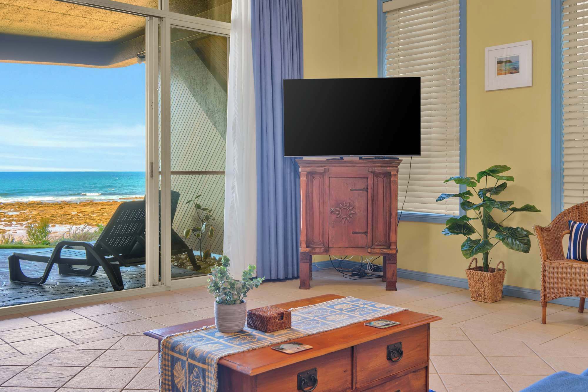 Een kamer met een televisie op een houten kast, een potplant en uitzicht op het strand.