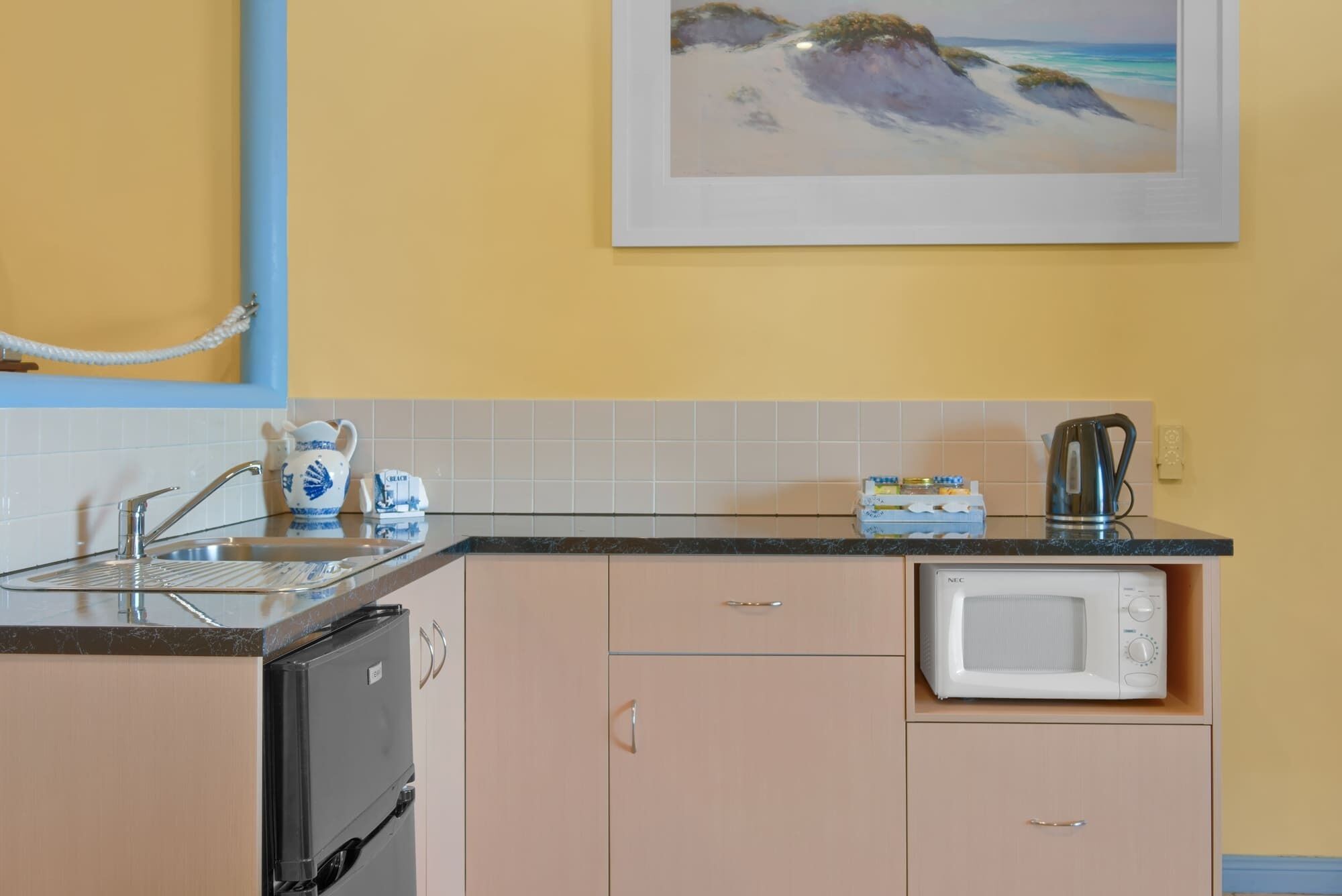 Een functionele keuken met een spoelbak, een magnetron en een kleine koelkast.