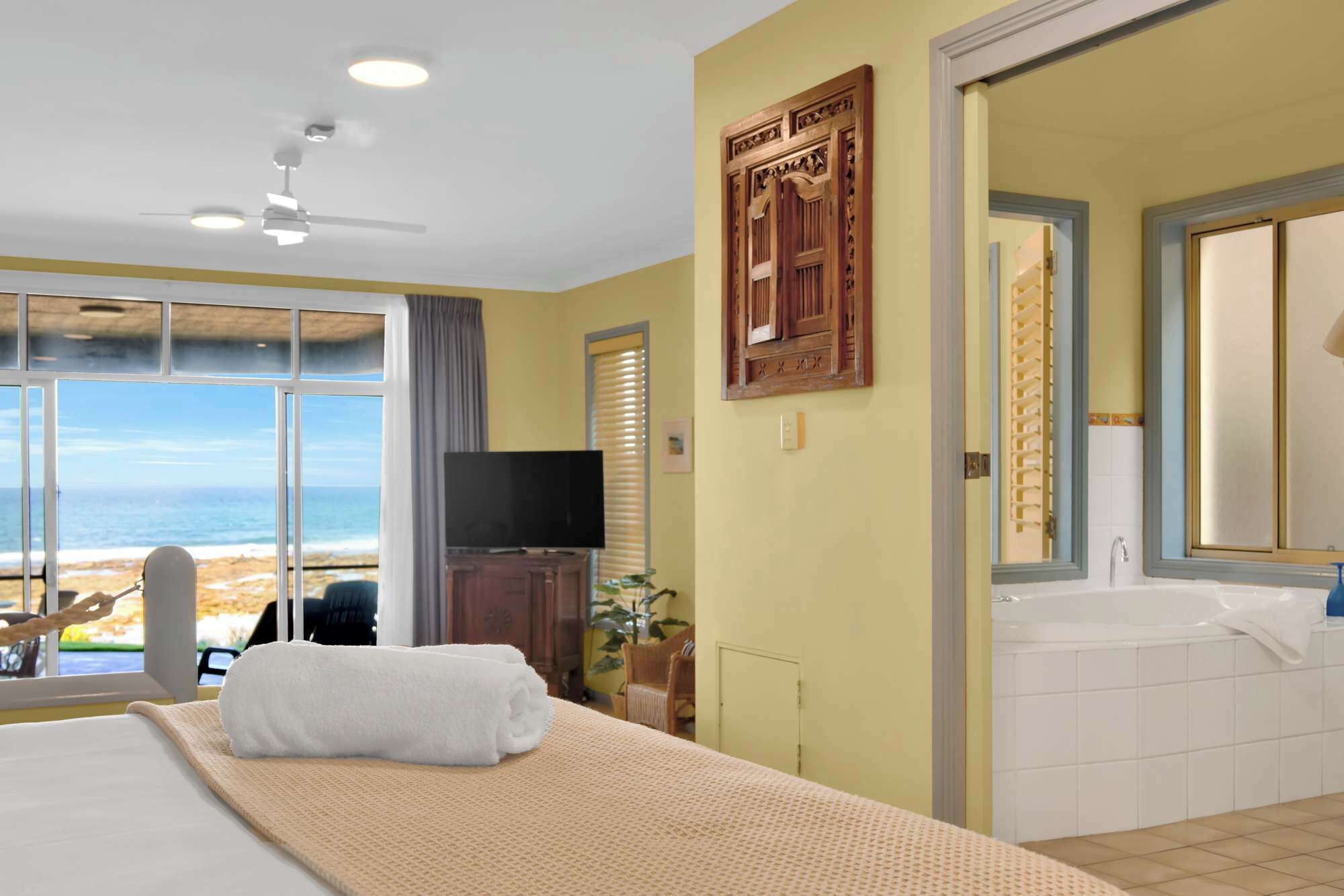 Une chambre d’hôtel avec un lit, une télévision, une vue sur la plage et une salle de bain avec baignoire.