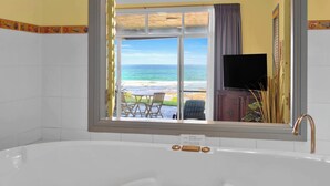 Un baño con una bañera grande, vistas a la playa y un televisor.