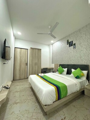 Un dormitorio con cama, escritorio, silla, armario, ventilador de techo y televisor.