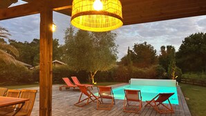 An outdoor deck with a pool, wooden furniture, and a hanging light fixture. - Prestigious golf and ocean villa rental (Moliets-et-Maa)