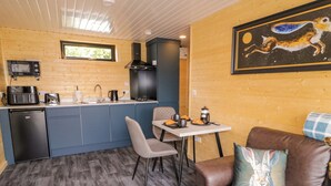 A compact kitchen with a microwave, sink, and coffee maker. There's a dining table with chairs and a brown leather sofa with a cushion. - Alken The Hare (Bushmills)