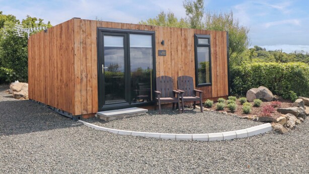 A wooden cabin with a sliding glass door, two wooden chairs, and a gravel driveway. - Alken The Hare (Bushmills)