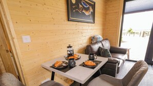 A cozy room with a wooden wall, a painting, a table with croissants, a coffee pot, and a couch. - Alken The Hare (Bushmills)