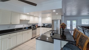 A modern kitchen with white cabinets, a black countertop, and a stainless steel refrigerator. - Sunset Key Escape Waterfront Pool Home with Dock and Sunset Views (Marathon)