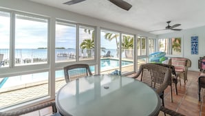 A spacious room with a large window overlooking a pool and the ocean. There are wicker chairs and a table with a glass top. - Sunset Key Escape Waterfront Pool Home with Dock and Sunset Views (Marathon)