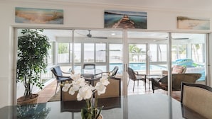 A glass-enclosed dining area with a view of a pool and beach. - Sunset Key Escape Waterfront Pool Home with Dock and Sunset Views (Marathon)