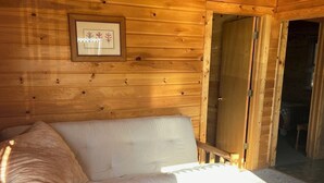 Puinen mökki, jonka sisustuksessa on sohva, pieni puinen pöytä ja seinällä oleva kehystetty kuva.
