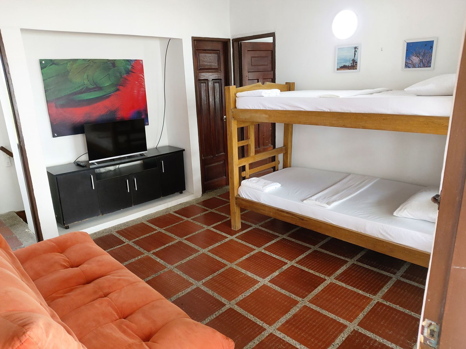 Habitación con literas, un televisor sobre un mueble negro, una puerta y piso de baldosas.