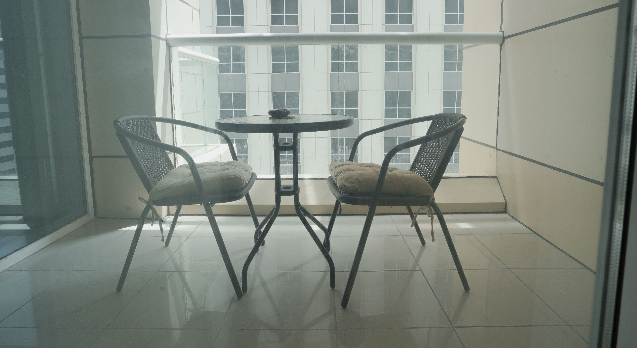 A balcony with two wicker chairs and a small round table.