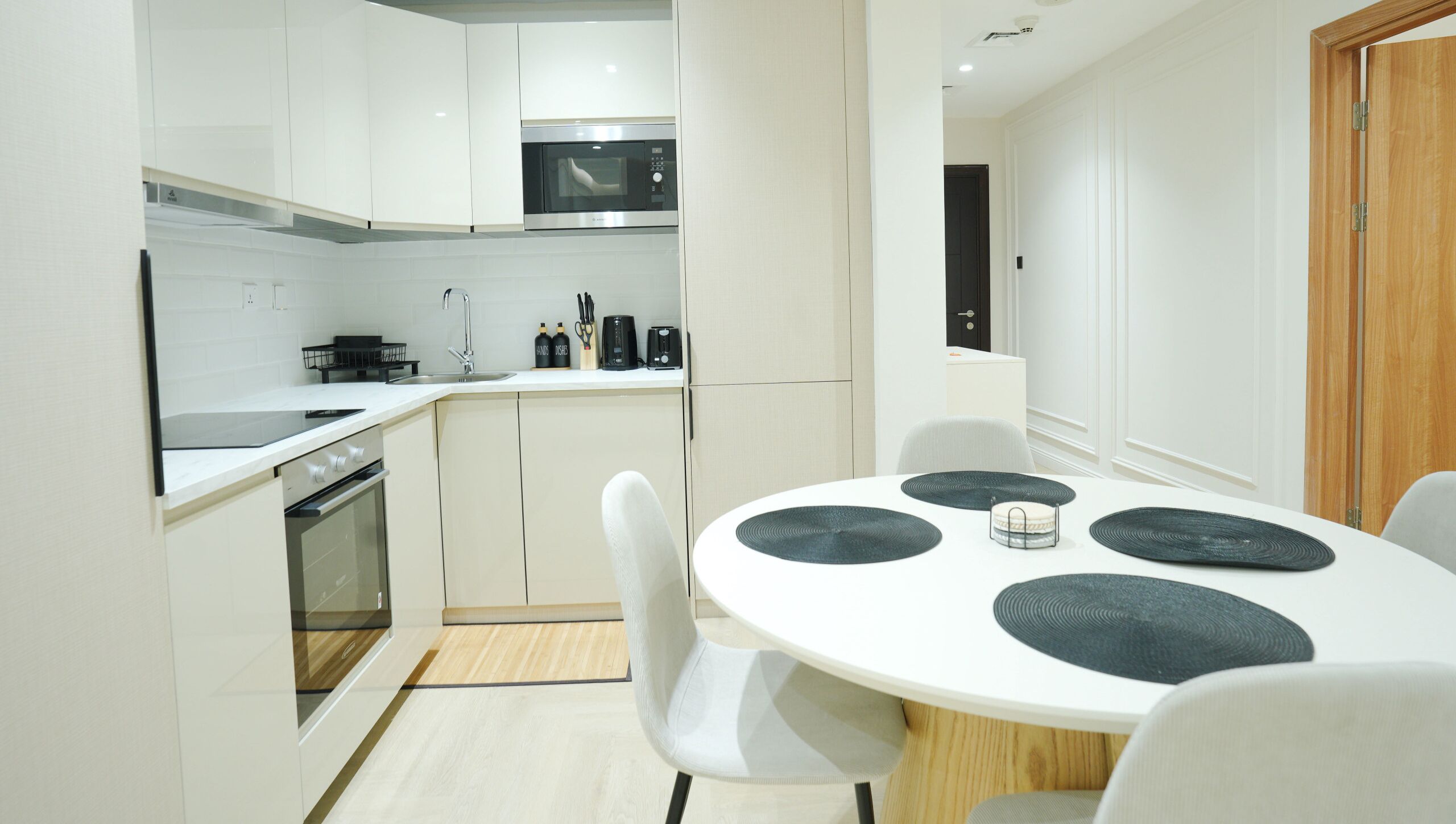 Una cocina moderna con armarios blancos, un microondas y una estufa. Hay un comedor con una mesa y sillas blancas.