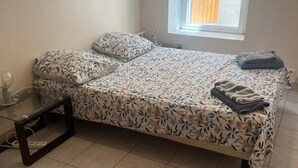A single bed with a floral bedspread, a small bedside table, and a window with blinds.