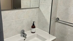 A bathroom with a white sink, a mirror, and a hand soap bottle.