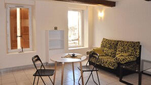A room with a round table, two chairs, a sofa, a bookshelf, and a window with curtains.