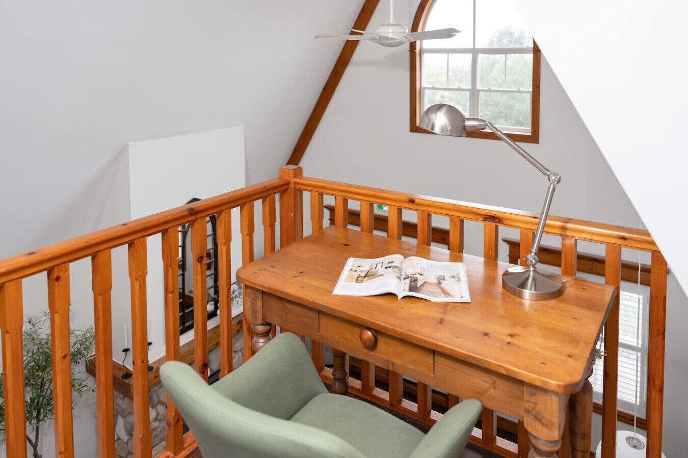 A wooden desk with a lamp and a magazine, a green chair, and a wooden railing.