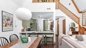 A modern kitchen with white cabinets, a wooden dining table, and a staircase with wooden railings. - The Fairway: Home with Ski, Golf + Mountain Views (The Blue Mountains)