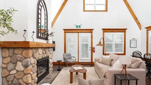 A cozy living room with a stone fireplace, wooden beams, a sofa, a coffee table, and a lamp. - The Fairway: Home with Ski, Golf + Mountain Views (The Blue Mountains)