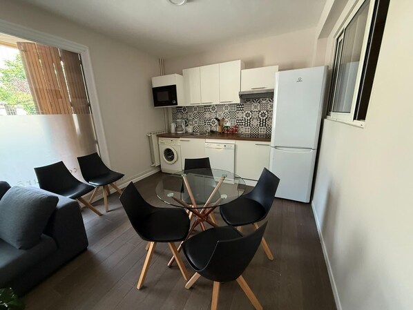 A compact kitchen with a microwave, washing machine, and refrigerator. There is a glass table with four chairs and a sofa with cushions. - Apartment in the heart of the Avignon festival (Avignon)