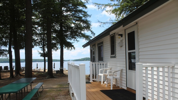 A cabin with a deck, picnic tables, and a view of the lake. - Lakeside 2-bedroom w/ AC sleeps 5. Quiet Beach in lovely Naples. (Naples)