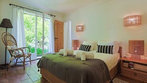 A bedroom with a large bed, a chair, a nightstand, and a window with curtains.