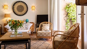 A cozy living room with a wooden coffee table, wicker chairs, a TV, and a large decorative wall piece.