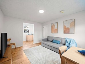 A modern living room with a grey sofa, a wooden dining table, and a TV stand.
