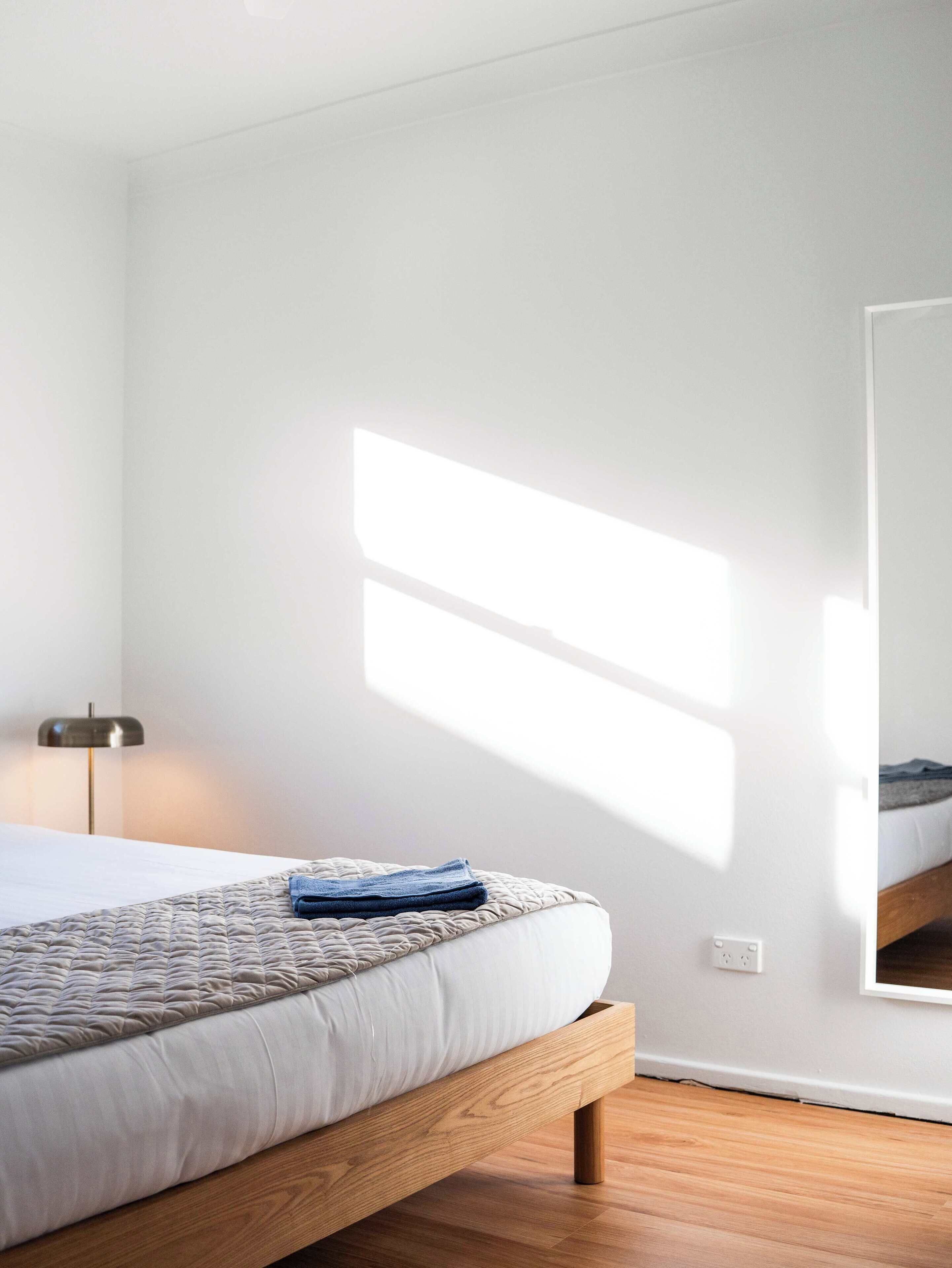 A bedroom with a bed, a bedside lamp, and a large mirror on the wall.