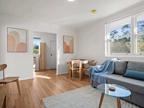 A modern living room with a sofa, a glass coffee table, and a dining area with wooden chairs and a table.