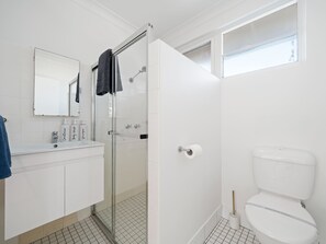 A bathroom with a glass-enclosed shower, a white toilet, and a sink with toiletries.