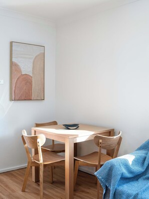 A dining area with a wooden table and chairs, a bowl on the table, and a blue blanket on the floor.