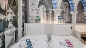 A hotel room with two beds, a geometric wall design, and a view of a stone building with arches. - Hotiday Como Paoli (Como)