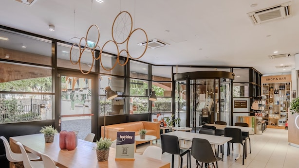 Un café moderno con pared de vidrio, mobiliario de madera y una sección de 'Shop & Bar'.