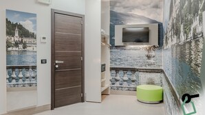 Un baño moderno con puerta de madera, televisor montado y una fuente decorativa.