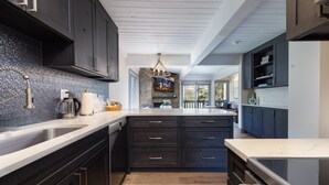 A modern kitchen with dark cabinetry, a large island, and a stone backsplash.