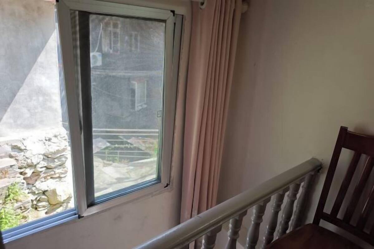 Une pièce avec une fenêtre, une chaise en bois et un mur de pierre à l’extérieur.