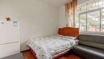 Una camera da letto con un letto, un divano, un frigorifero e una finestra con tende.