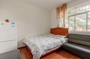 Un dormitorio con cama, sofá, refrigerador y ventana con cortinas.
